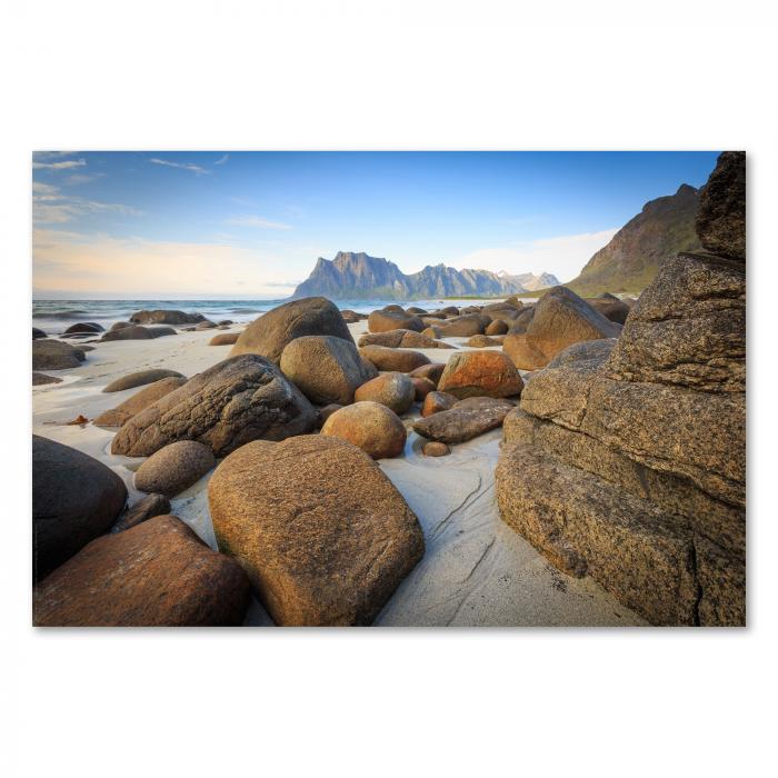 Runde Felsen liegen auf Sandstrand, majestätische Berge erheben sich im Hintergrund.